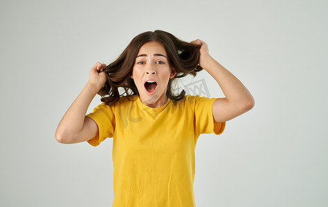 穿着黄色T恤的情绪化女人拿着头发工作室的裁剪视图