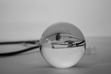 渐变玻璃背景摄影照片_水晶玻璃球体在灰色渐变背景下显示内部医疗听诊器。