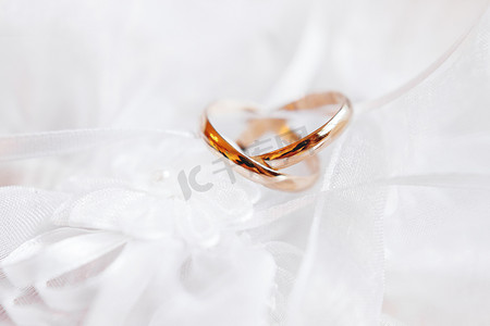 一对金色结婚戒指在蕾丝丝绸面料上与织物花。