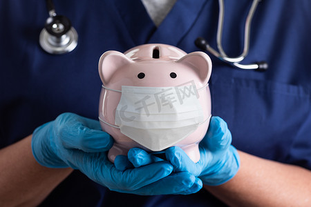 医院财务摄影照片_医生或护士戴着手术手套拿着存钱罐，戴着医用面罩。
