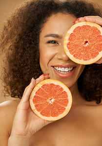 米色背景下，混血年轻女子在摆着切成两半的葡萄柚姿势时看上去很开心的肖像