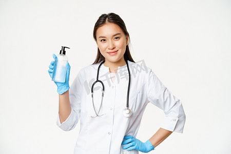 亚洲女医生的肖像，医生推荐用于预防covid-19的洗手液，拿着带橡胶手套的瓶子，白色背景