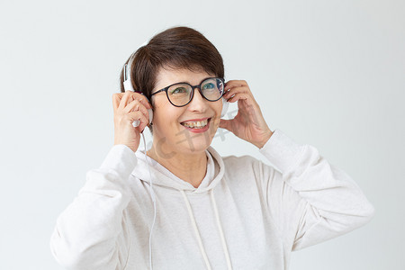 大观念摄影照片_爱好、兴趣和人的观念 — 40-50岁的美丽女性在白色背景下用大耳机听音乐