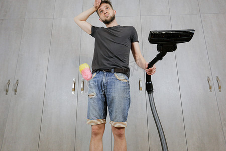 整理客厅摄影照片_一个有吸尘器的男人厌倦了打扫房子