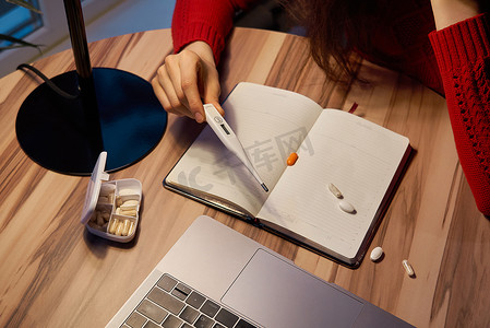 生病的妇女，桌上放着药丸和温度计，在家中用笔记本电脑工作，进行隔离。