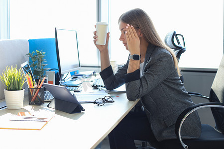 女性疲惫摄影照片_坐在工作地点，手里拿着纸杯的女商人看起来很疲惫的形象。