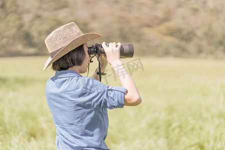 女人戴帽子，在草地上拿着双筒望远镜