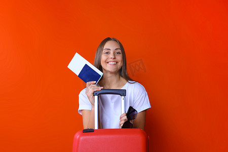 身穿夏季休闲服的年轻旅游女孩，带着太阳镜、红色手提箱、红色背景中突显的护照。