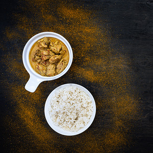 选择样式摄影照片_深色背景上简单的白色盘子里放着橙色辣味咖喱鸡和米饭。