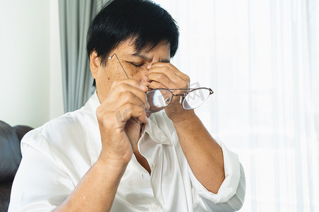 女性疲惫摄影照片_疲惫的老妇人摘下眼镜，读完纸质书后按摩眼睛。