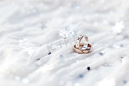 白色假日背景上的结婚戒指，闪闪发光的银色雪花，圣诞装饰品。