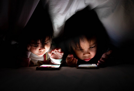 床上毯子下的智能手机上，亚洲小女孩和妹妹的肖像看起来很卡通。