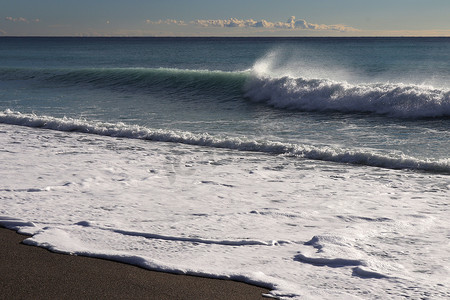 平静的海面摄影照片_平静的海面与飞溅的波浪和沙滩海景上的长泡沫。