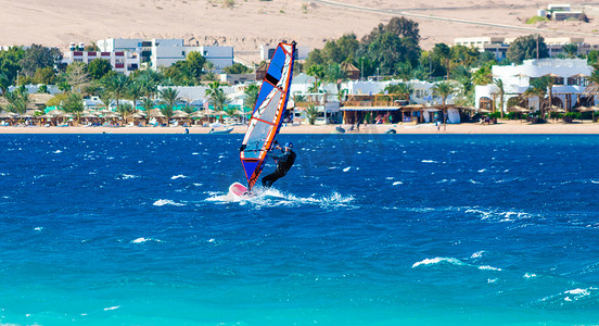 半岛酒店摄影照片_风帆冲浪者在海滩的背景上与酒店一起骑行，