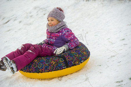 冬天，一个穿着紫色衣服和充气圈的小女孩在街上从山上骑下来