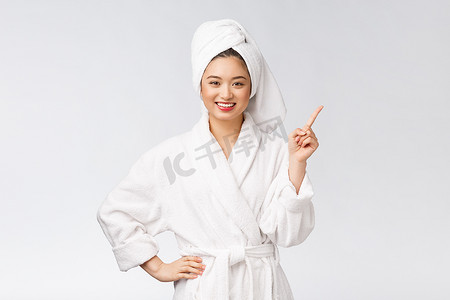 年轻女子的美丽肖像展示并指向空的复制空间，穿着浴袍的亚洲美女。