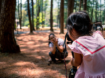亚洲小孩使用相机在泰国清迈的松林里为她的母亲拍照。