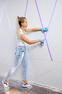 年轻女子站在梯子上准备墙壁绘画，在墙上贴胶带。 