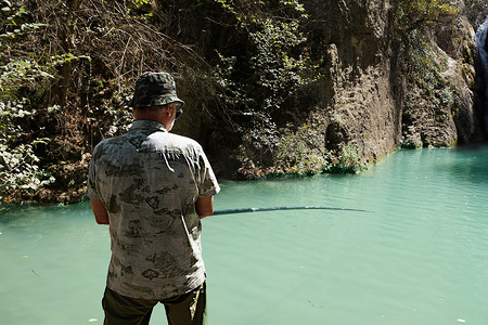 车子后视镜摄影照片_男人在有瀑布的山湖里钓鱼，后视