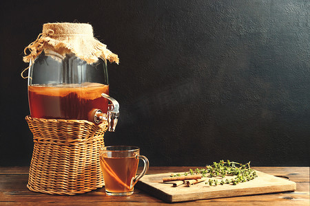 新鲜自制康普茶发酵茶饮料，装在带水龙头的罐子里，放在深色背景的杯子里