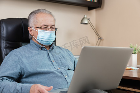 戴着面罩的老人在家里工作或在笔记本电脑上交流。