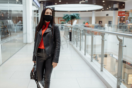 一个戴着医用黑色口罩的女孩沿着购物中心行走。