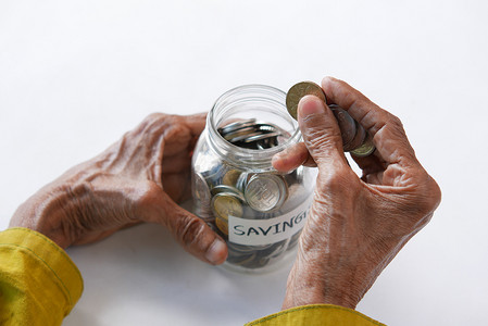 老年妇女将硬币放在桌子上的罐子里