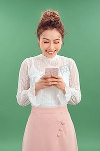 快乐的年轻亚洲女性站在绿色背景下使用智能手机。