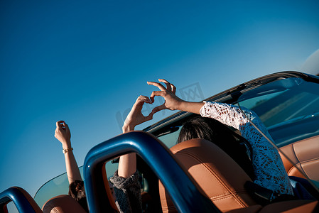 女性朋友举起手来驾驶敞篷车，玩得很开心