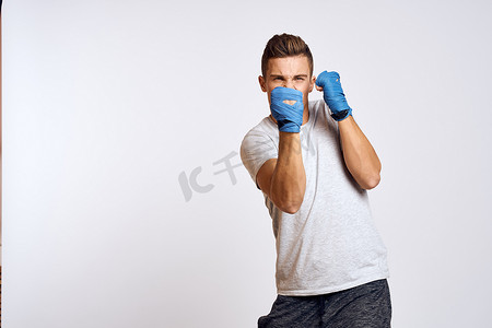 活动浅色背景摄影照片_戴着蓝色手套的运动男拳击手在浅色背景裁剪视图中练习拳击