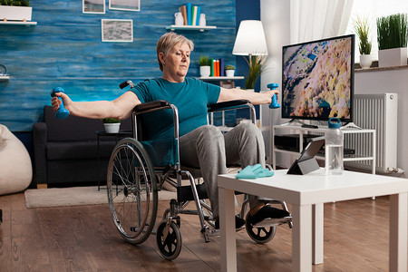 课程培训摄影照片_轮椅上的残疾老年妇女伸展手臂肌肉锻炼身体抵抗力