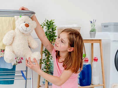 小女孩把泰迪熊挂在烘干机上