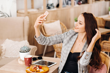 一个商务女孩坐在咖啡馆里自拍，一个咖啡店里的女孩微笑着用智能手机自拍