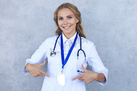 微笑的金发女医生穿着制服站在灰色背景中，在徽章上显示她的名字。