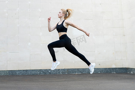 运动和健身概念年轻成年白人女运动员在户外灰尾墙背景下跳高
