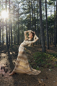丝质裙子摄影照片_一个女人穿着裙子在大自然中跳舞，靠在森林的针叶树中