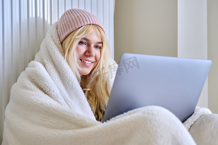 冬季寒冷季节冰冻的青少年，用毯子帽取暖，看着笔记本电脑