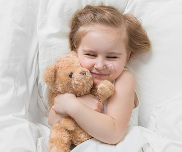 女孩抱着她的棕色泰迪熊，躺在床上