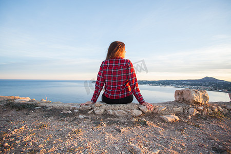 旅行、冒险和孤独的概念 — 一个女孩坐在悬崖边，望着大海