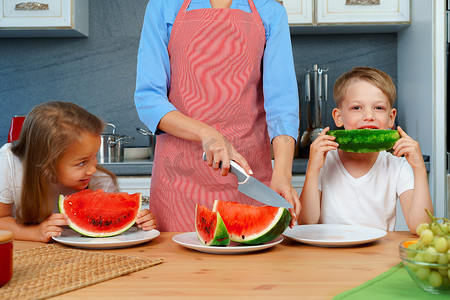 甜蜜的家庭，母亲和她的孩子在厨房里吃西瓜玩得很开心