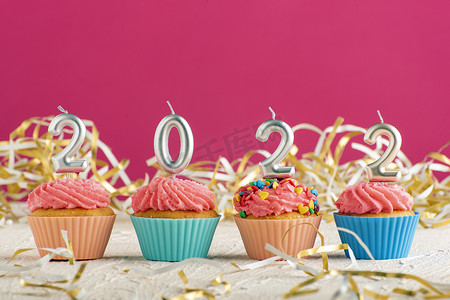 粉红色背景上数字 2022 形式的节日纸杯蛋糕和蜡烛。
