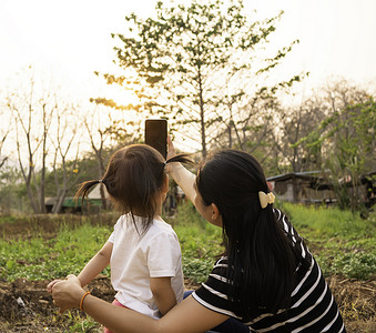 女孩与母亲合影摄影照片_亚洲小女孩在日落背景下在花园里与母亲合影的后视图。
