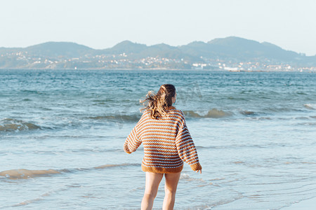 阳光明媚的日子里，海滩上戴着手术口罩的年轻女子穿着一件有复印空间和快乐资质的毛衣