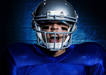 蓝墙背景下戴着头盔尖叫的好斗的美式足球运动员