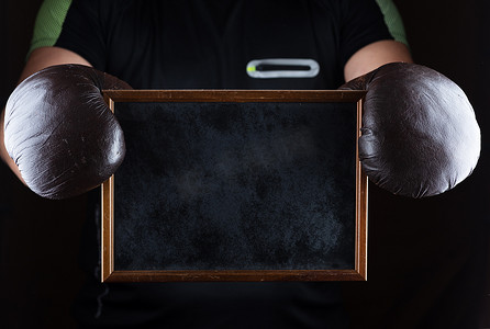 拳击黑摄影照片_戴着拳击手套的男人的手握着一个空的黑框