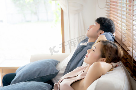 年轻的亚洲夫妇微笑着在客厅的沙发上放松舒适