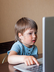 孩子的困惑摄影照片_好奇的蹒跚学步的男孩探索笔记本电脑并按下 c 上的按钮