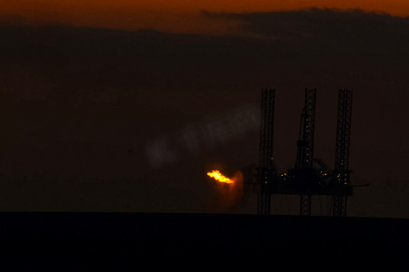 石油燃烧摄影照片_在日落时的石油平台与燃烧的火炬。石油平台的牵引。