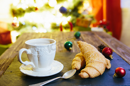 木桌上放着热巧克力的杯子，圣诞树背景上有圣诞装饰