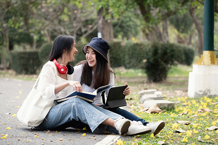 校园摄影照片_两个快乐的学生在公园的校园里坐着聊天。